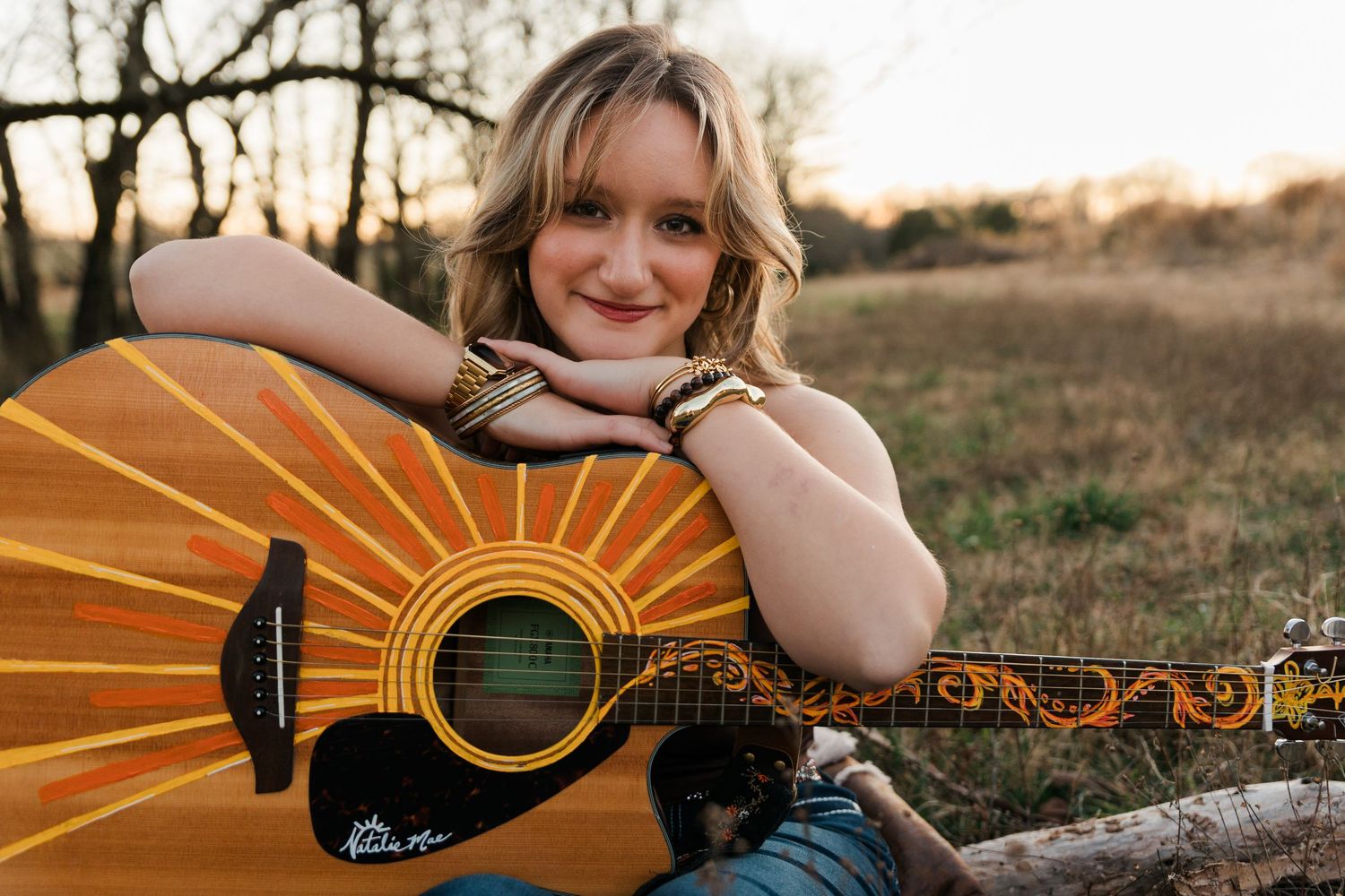 Acoustic guitar with decorative sunburst design rests against rustic outdoor setting during golden hour.