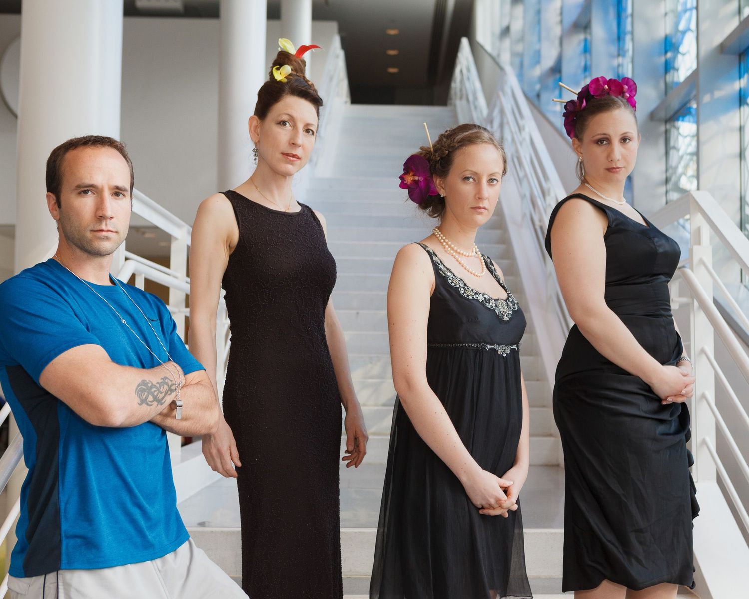 Row of dancers in black and blue outfits posing against a bright window background.