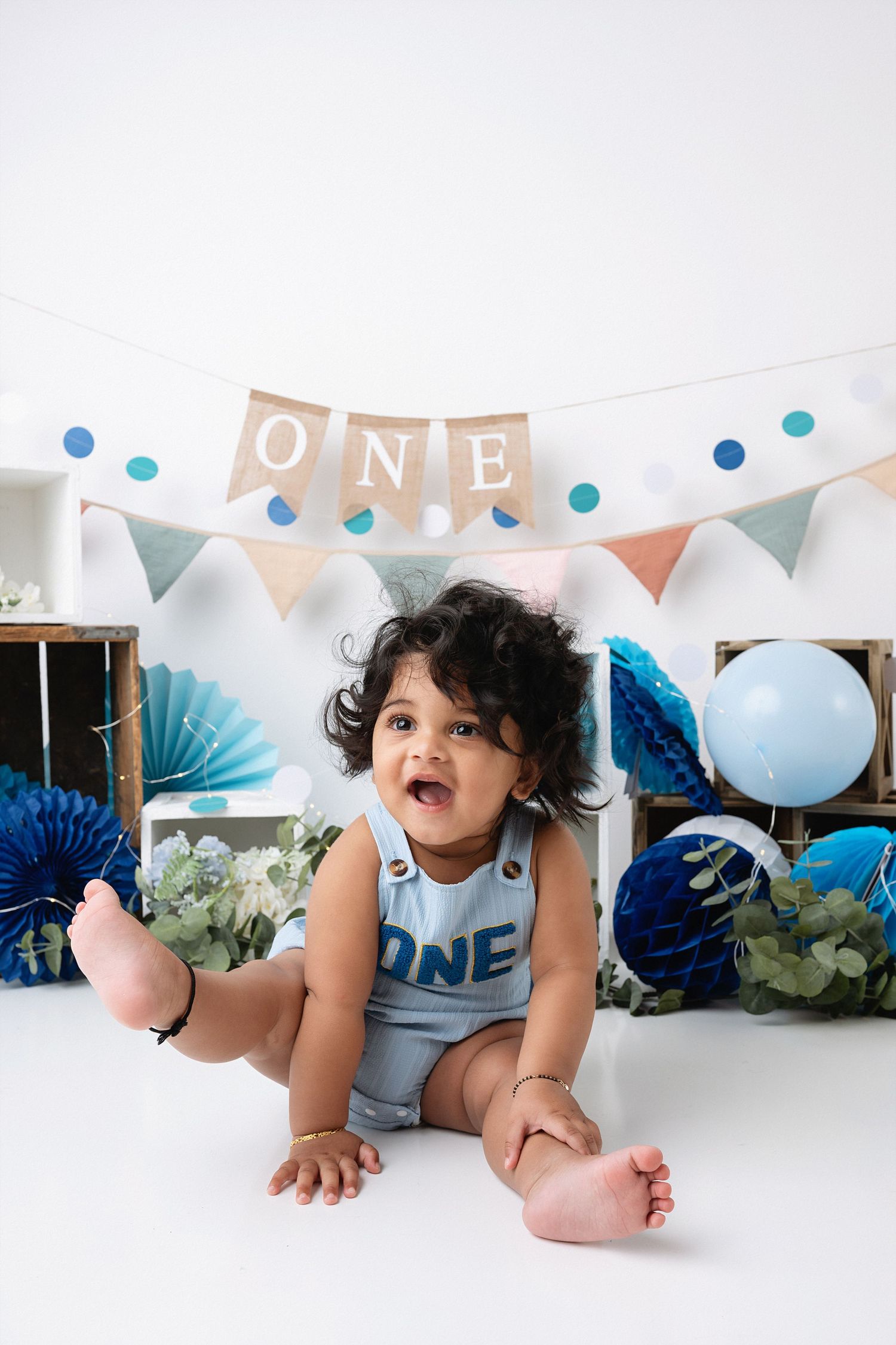 First birthday party setup with blue and white decorations, balloons, and bunting banner spelling ONE.