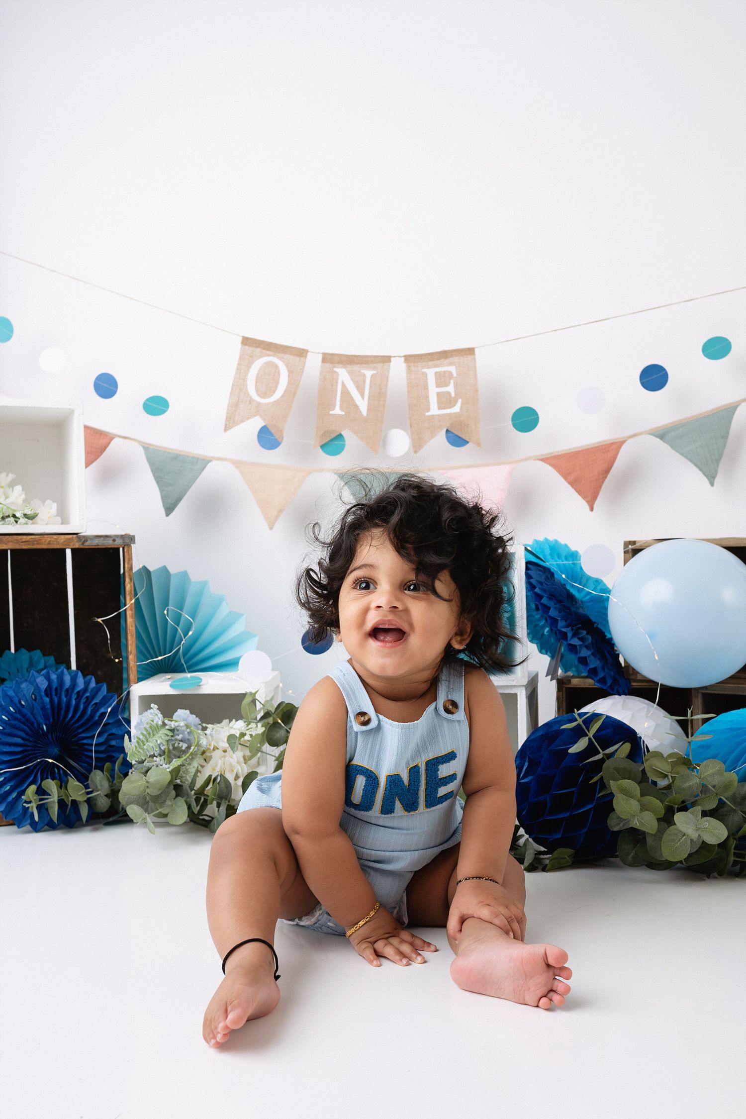 First birthday party setup with blue and white balloons, paper fans, and bunting decorations for a baby milestone celebration.