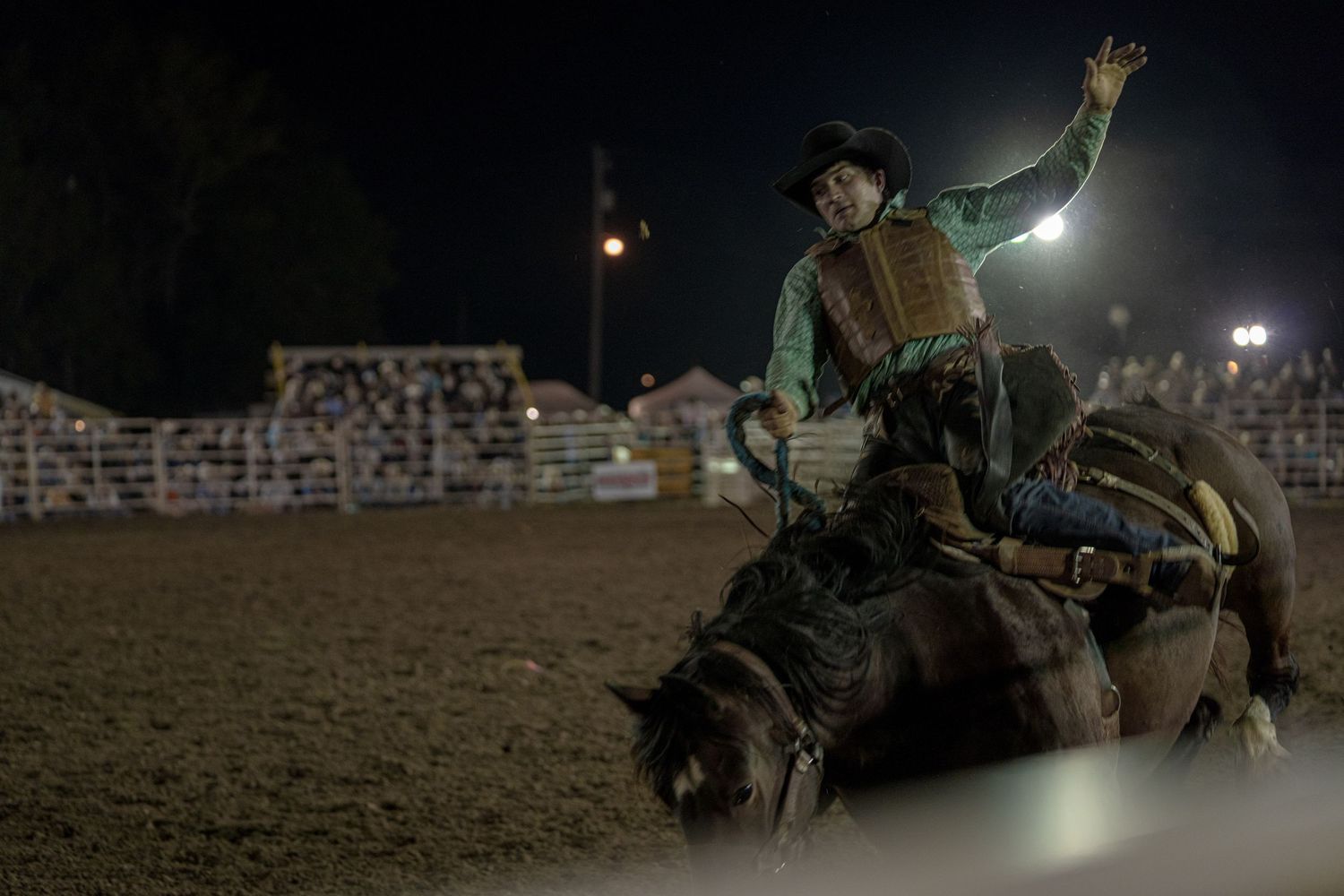 Rodeo performer riding a bucking horse at night under arena lights.