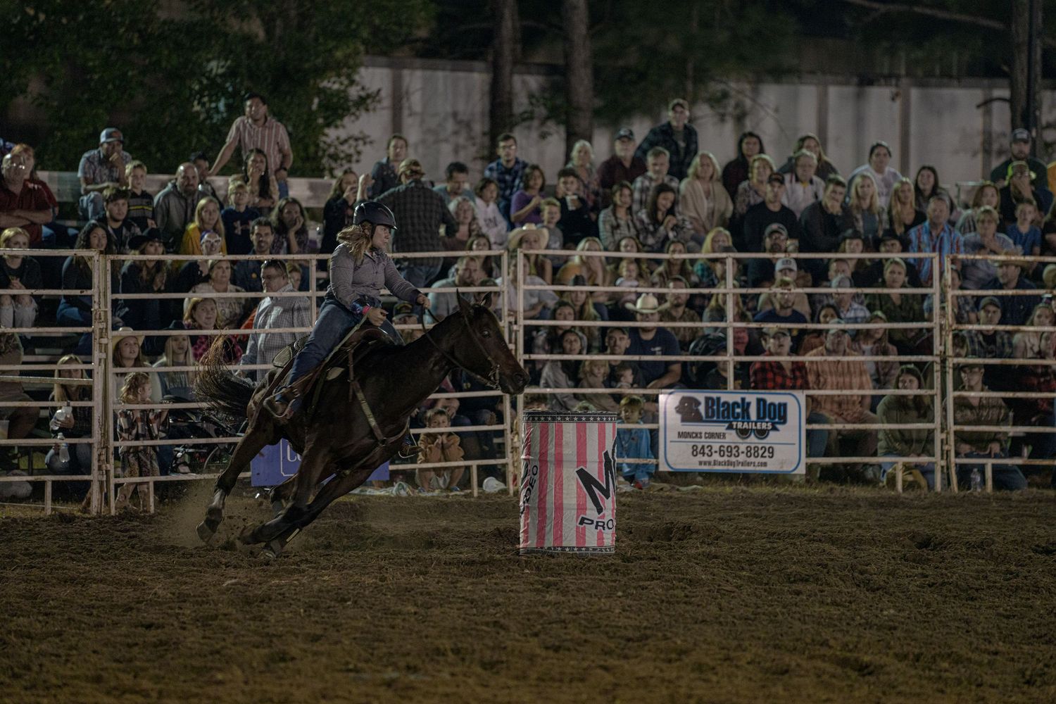 Rodeo scene showing multiple cowboys riding horses in an arena with spectators in the background.