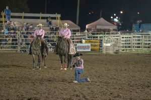Rodeo competitors in an arena at night with white fencing and stadium lights.