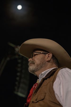 Side profile of a cowboy in traditional western attire with a cowboy hat against a dark background.