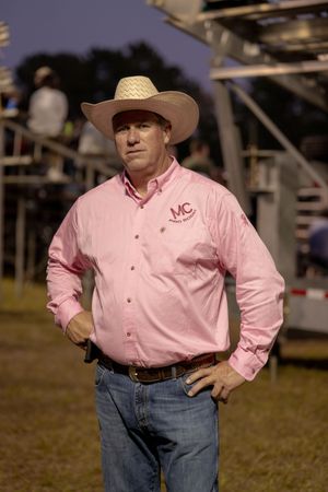 Person wearing a pink button-down shirt and cowboy hat at a rodeo event.