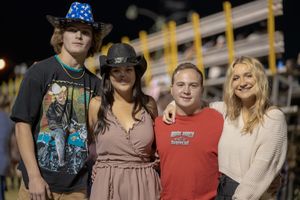 Spectators gather along the fence at a nighttime rodeo event.