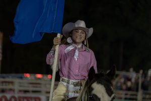 A series of equestrian riders in pink and white outfits compete in a western rodeo event at night.