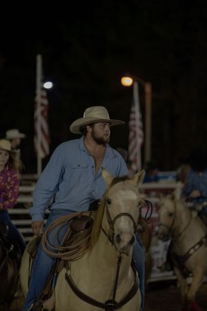 Horseback rider in blue shirt and cowboy hat during nighttime rodeo event.