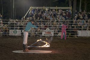 Rodeo clown performing with fire during nighttime arena show.