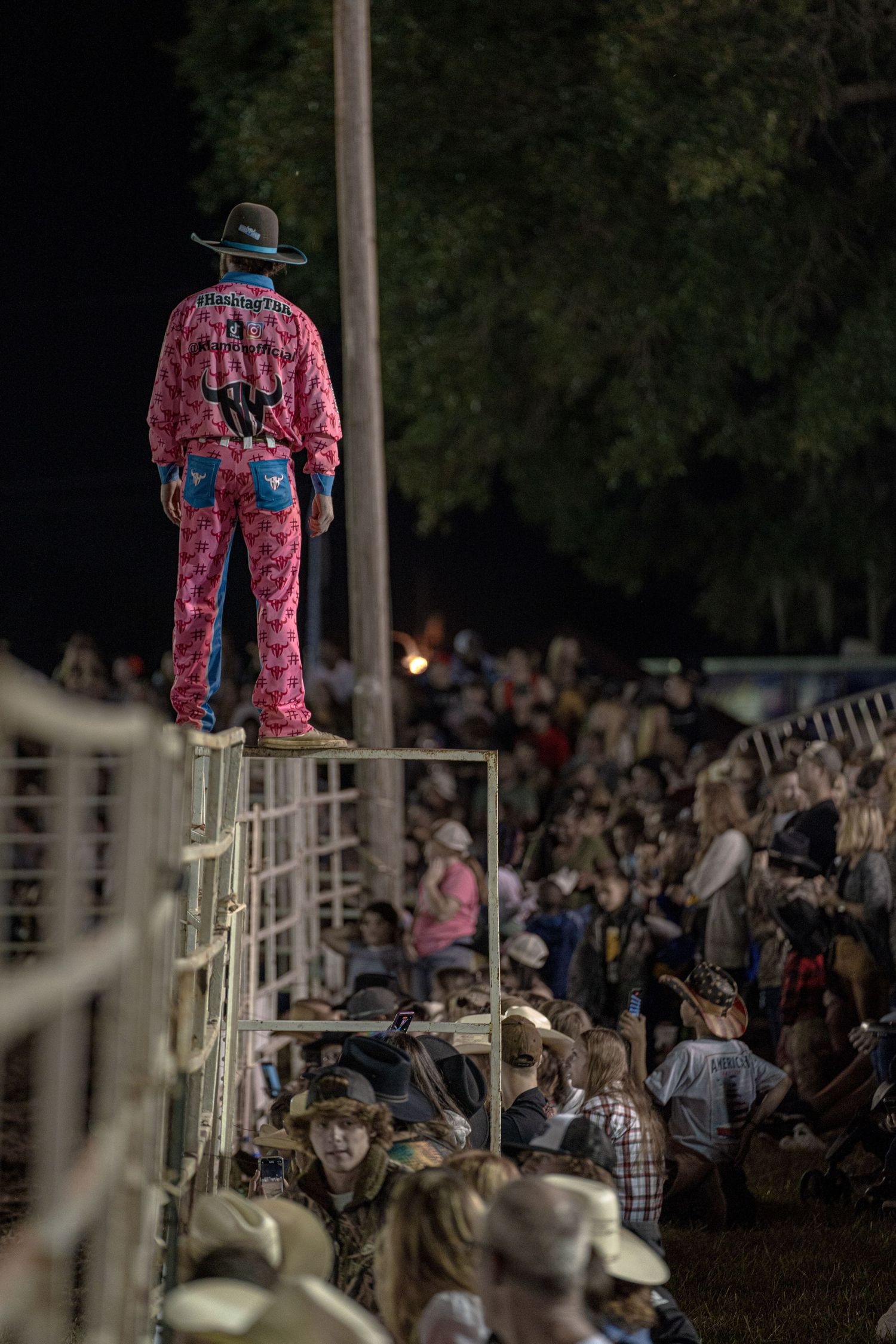 Rodeo entertainer standing on elevated platform above crowd wearing colorful outfit.
