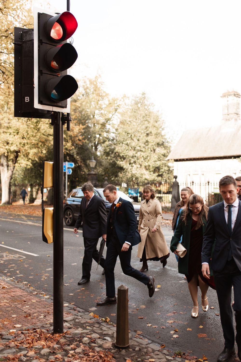 People playfully jumping and posing near a traffic light on a street with scattered fall leaves.