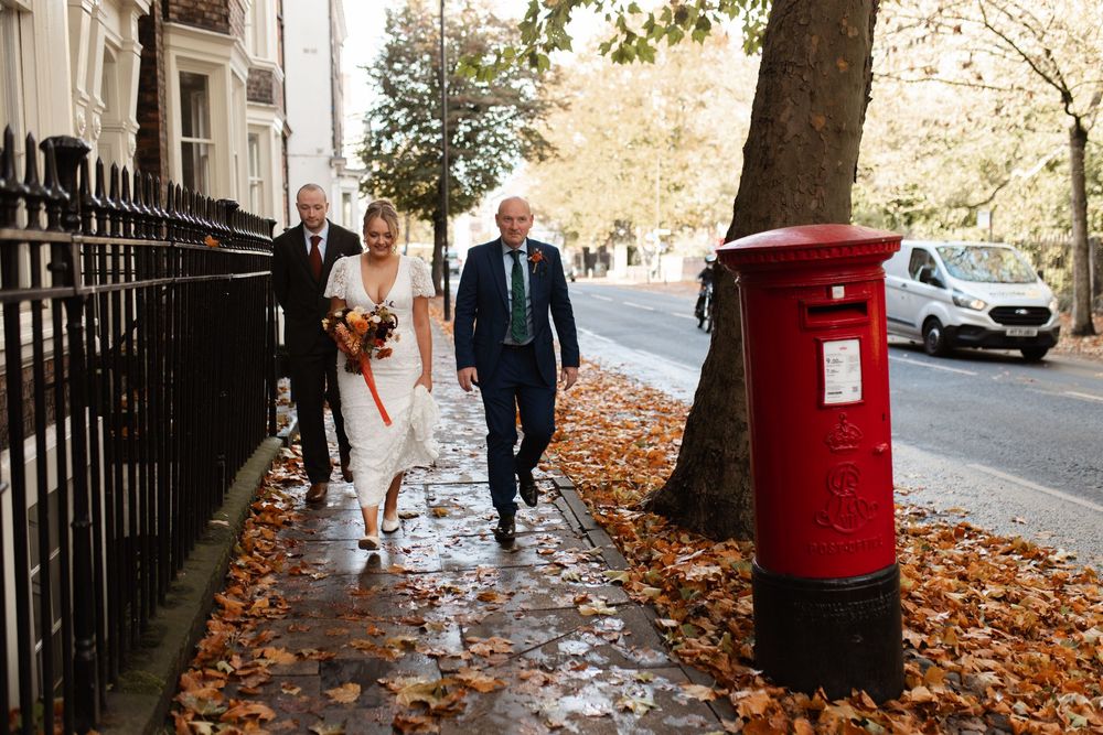 Autumn wedding photos captured near a red British post box with fallen leaves scattered on the ground.