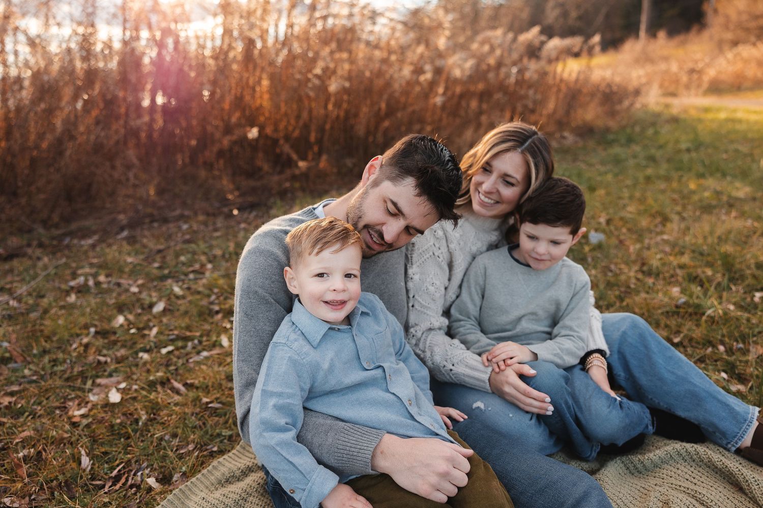 Intimate family portrait outdoors at sunset with parents and two young children sharing a tender moment in nature.
