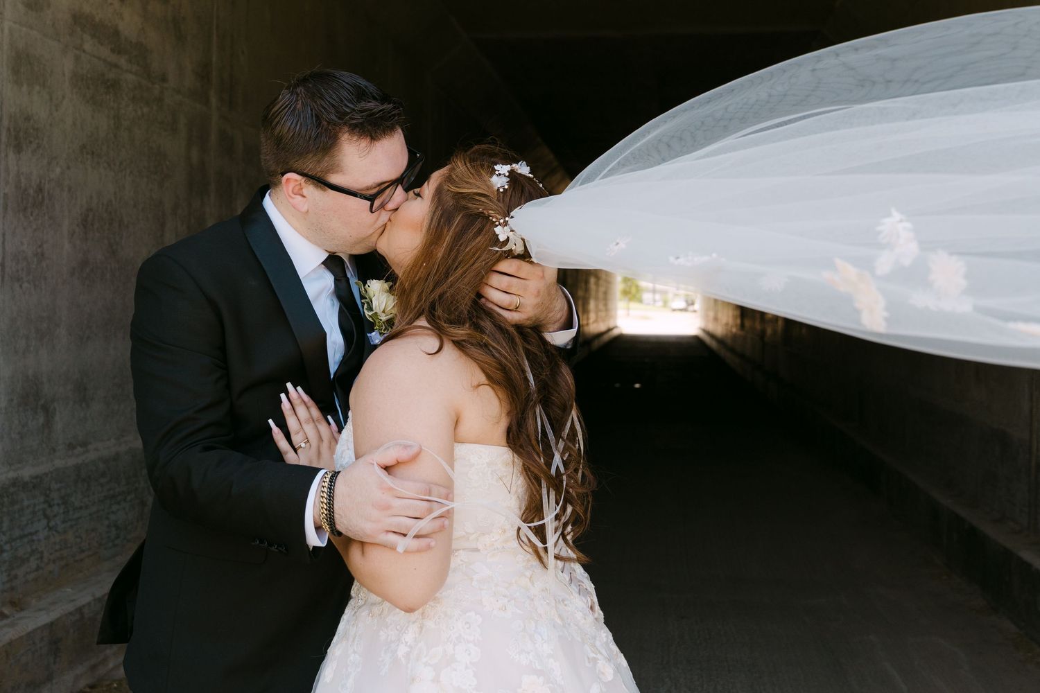 A romantic wedding couple embraces in an intimate moment with a long flowing veil.