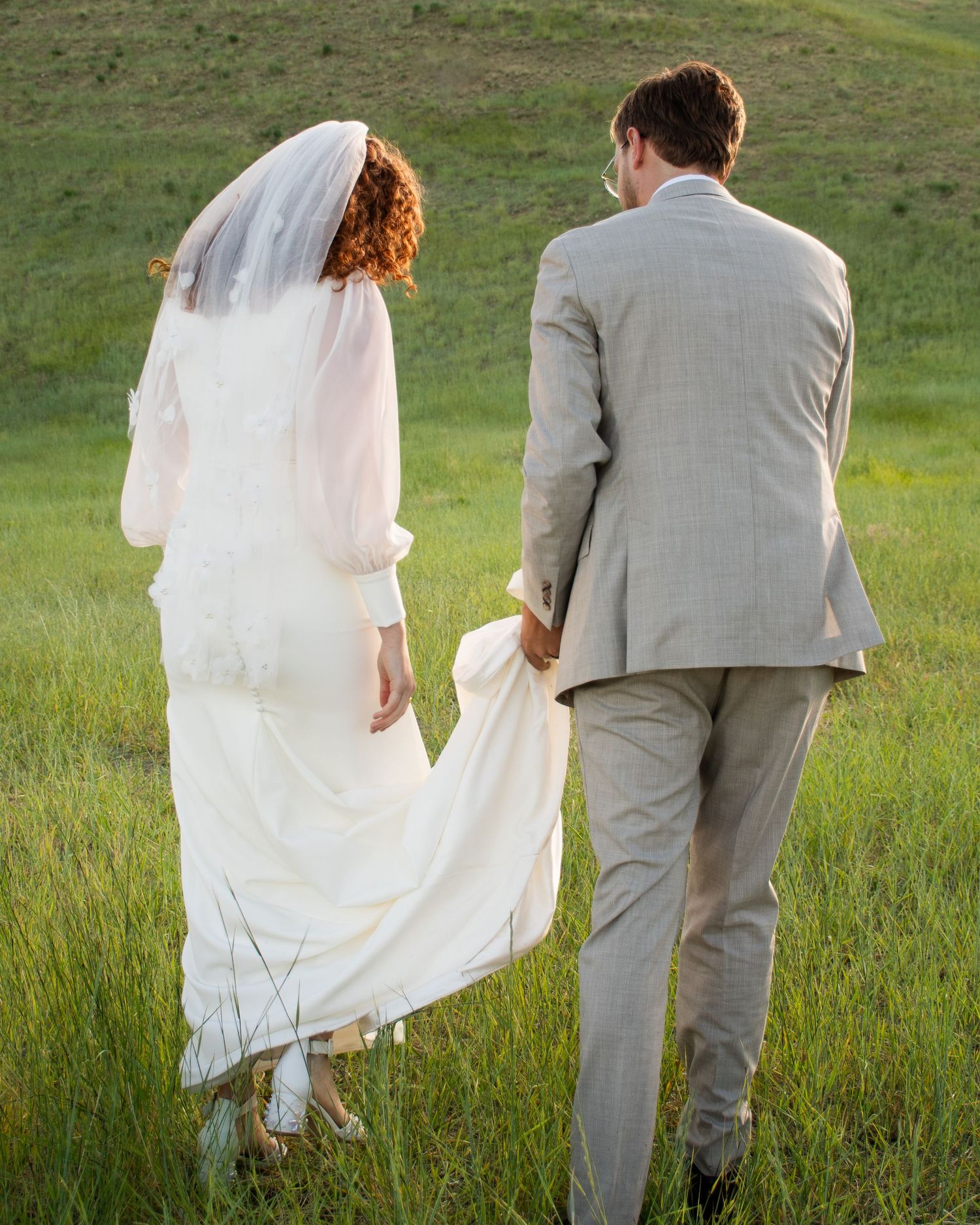 A couple walks together through a sunlit meadow of tall grass during a wedding photo session in Salt Lake City Utah.