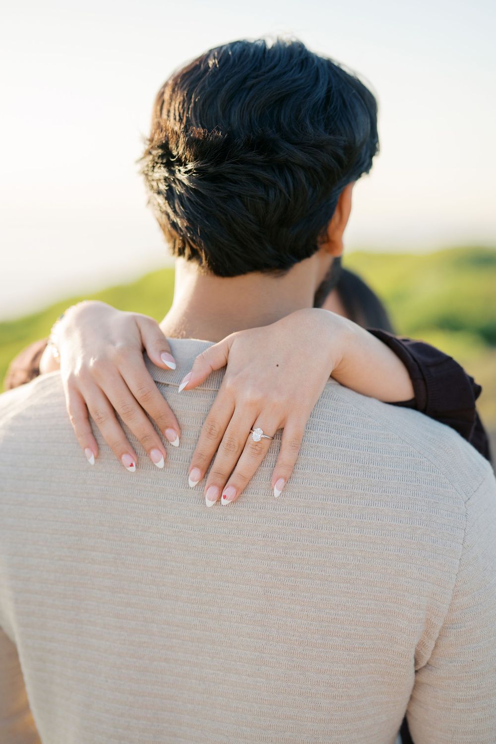 Close-up series of hands with engagement ring resting on a gray sweater shoulder during an outdoor photoshoot.