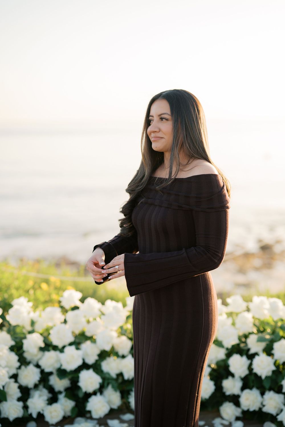 A person in a black off-shoulder dress poses in a series of photos against white flowers during golden hour.