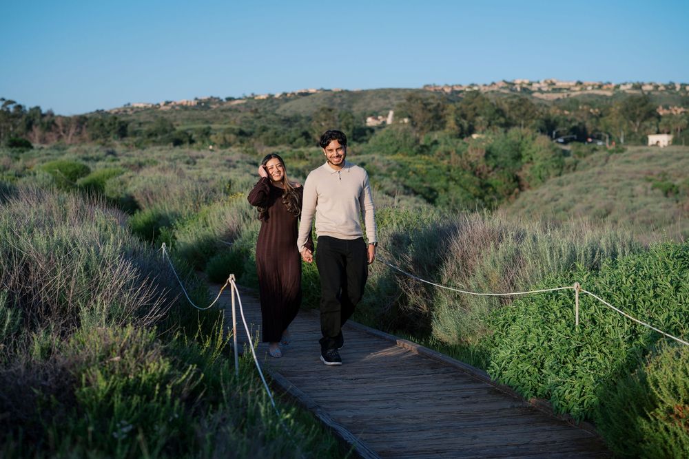 People walking along a winding boardwalk path through green wetland vegetation under blue sky.
