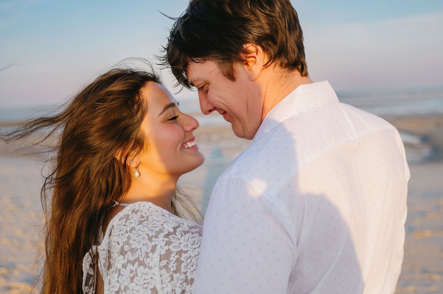 A tender moment between a couple on the beach with soft sunset lighting.