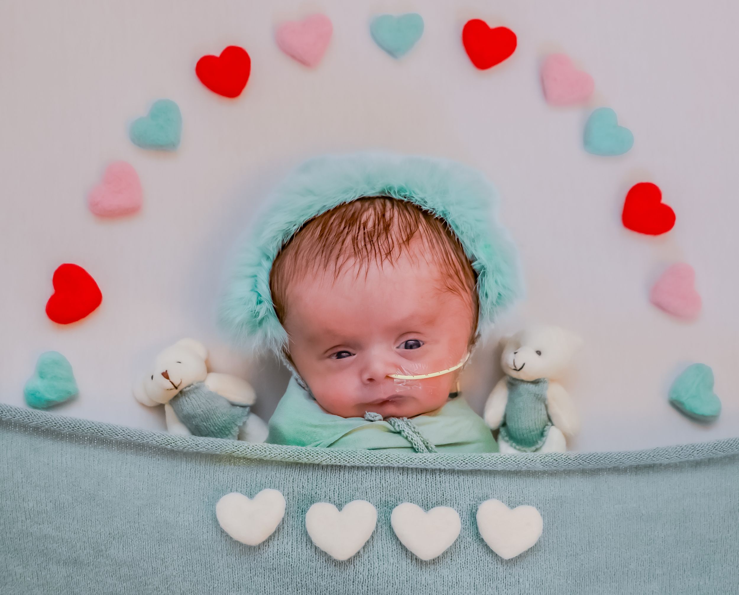 A newborn photography setup with red and blue heart decorations and small teddy bears.
