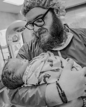 Healthcare worker in protective gear tenderly holds newborn baby in hospital setting.