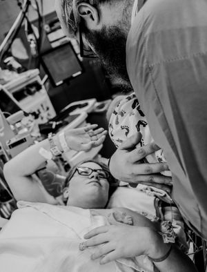 Black and white hospital photo showing intimate moment with newborn surrounded by medical equipment.