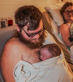 A tender skin-to-skin bonding moment with a newborn baby wrapped in white cloth.
