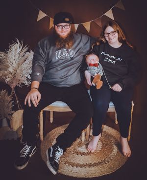 Family sitting on round woven mat during indoor photoshoot with festive bunting overhead.