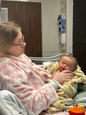 Hospital room scene showing tender moment between caregiver and newborn.