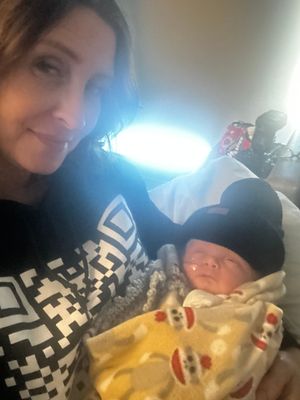 Cozy moment with newborn wearing black beanie and wrapped in patterned blanket.