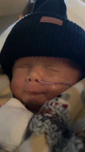 Baby wearing dark blue knit hat sleeping peacefully against soft blanket.