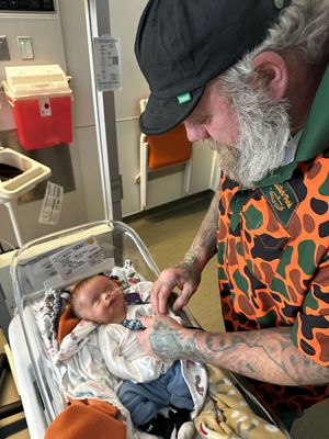 Person in camouflage jacket caring for newborn in hospital setting.