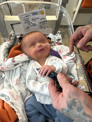 Newborn baby wearing white hospital clothing rests peacefully in a medical setting.