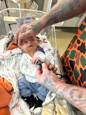 A small infant resting on orange bedding while being cared for by tattooed arms.