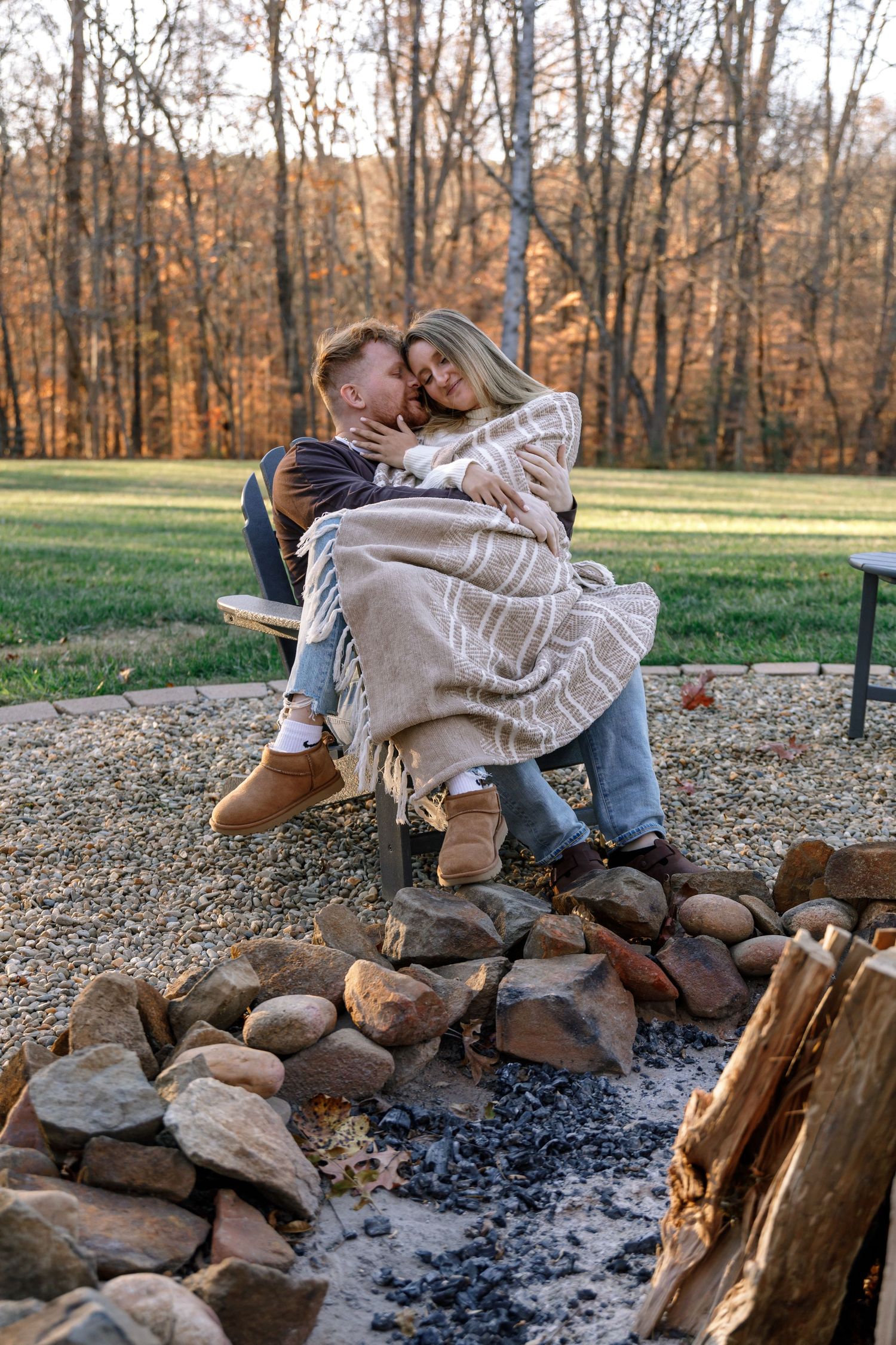 Couple sharing cozy moments by a rustic campfire with stacked firewood.