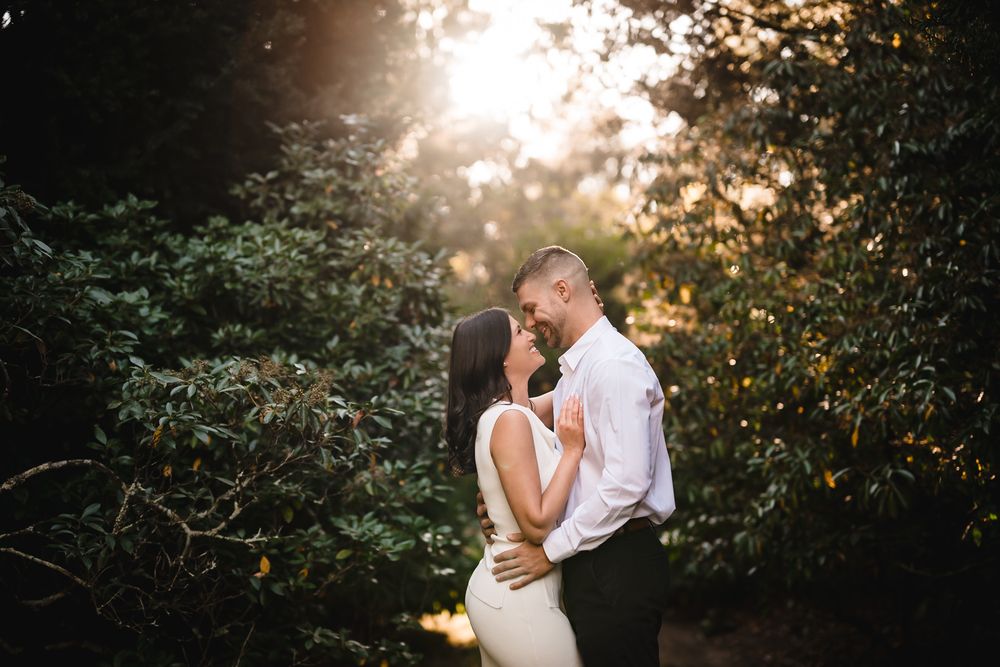 Romantic couple embraces during golden hour sunset photoshoot in a lush garden setting.