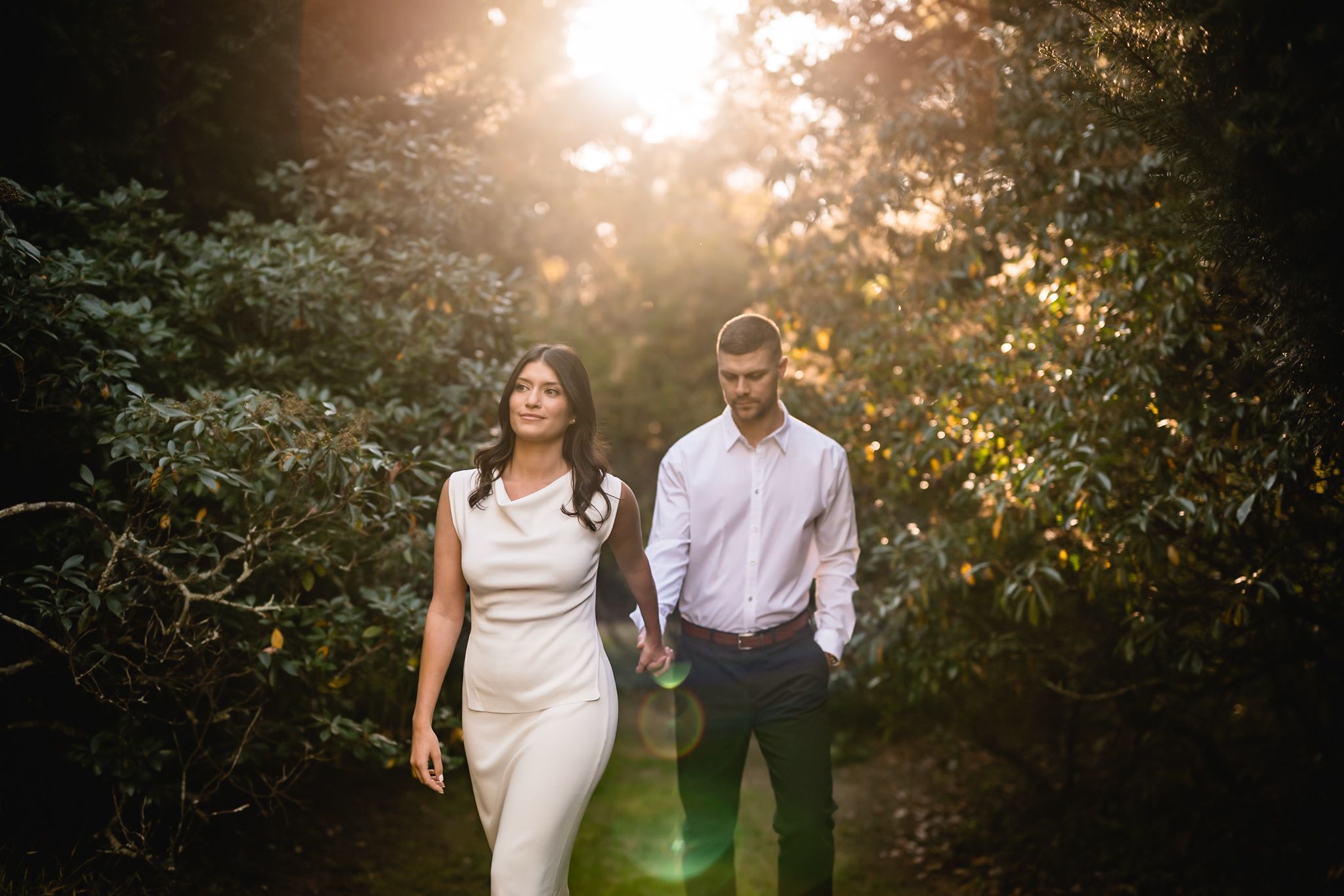 Couple shares intimate moment under glowing sunlight filtering through garden trees.