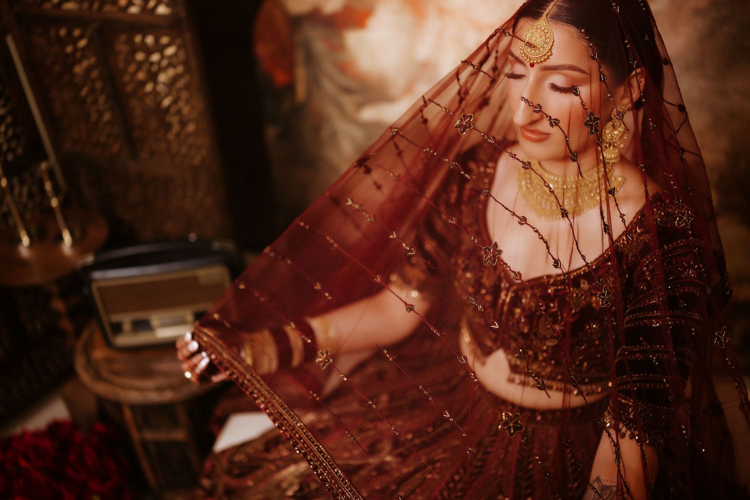 A woman in a burgundy lace dress poses elegantly in a romantic vintage-style photoshoot.