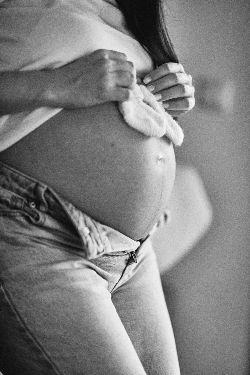Black and white close-up of pregnant belly with tiny baby booties held against it.