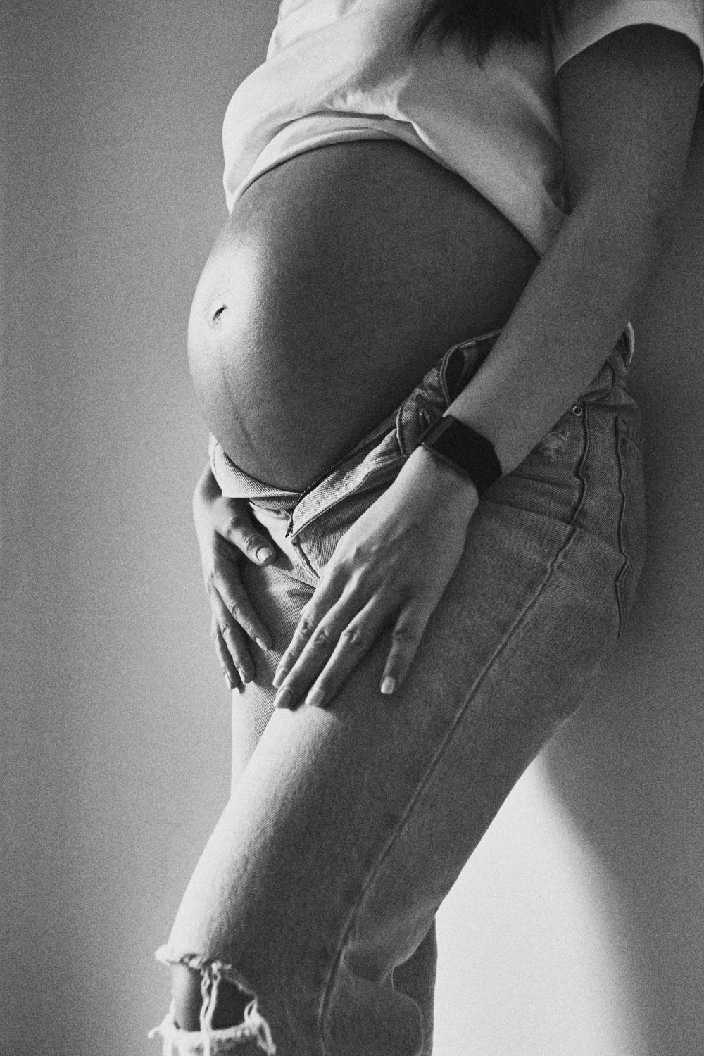 Black and white side profile of pregnant woman cradling her bare baby bump with both hands.