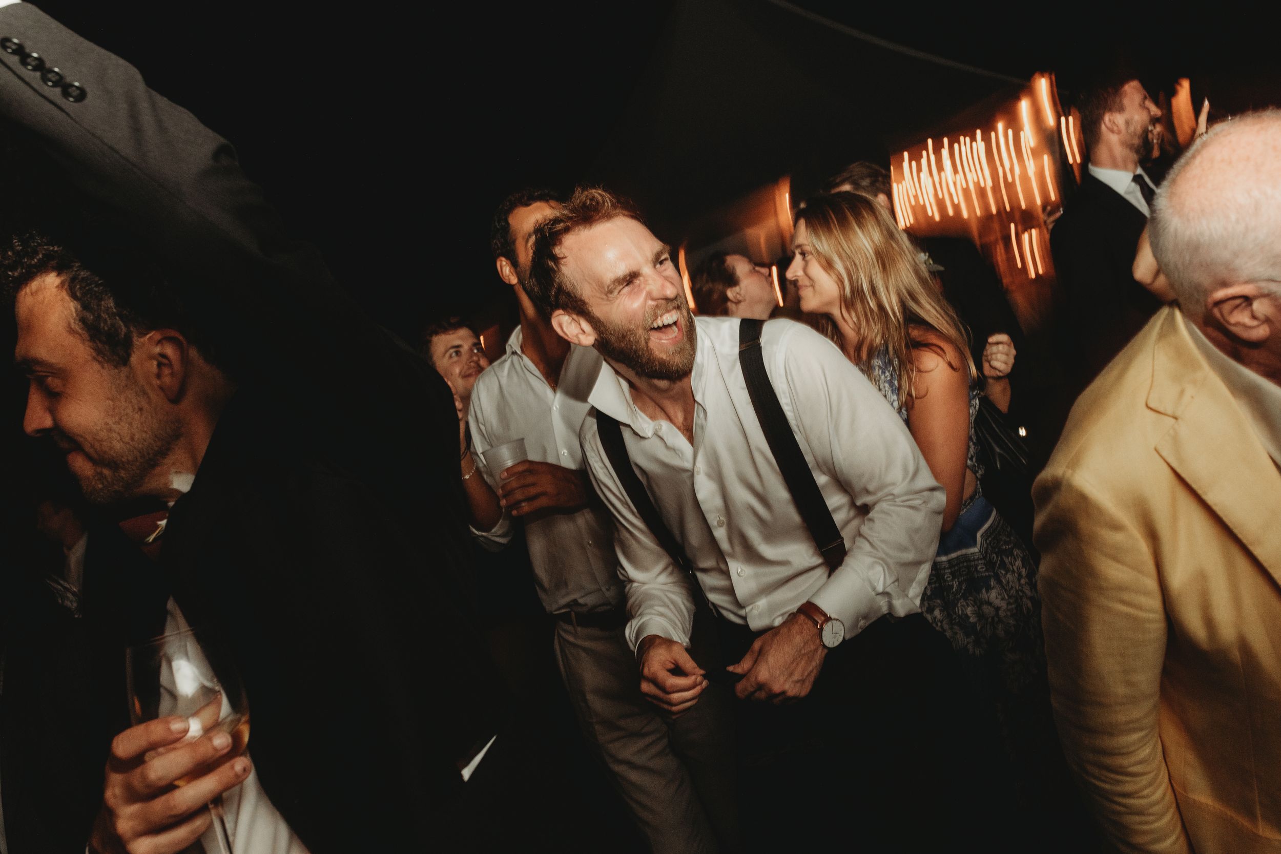 Wedding guests dancing and celebrating on a dark dance floor at a reception party.
