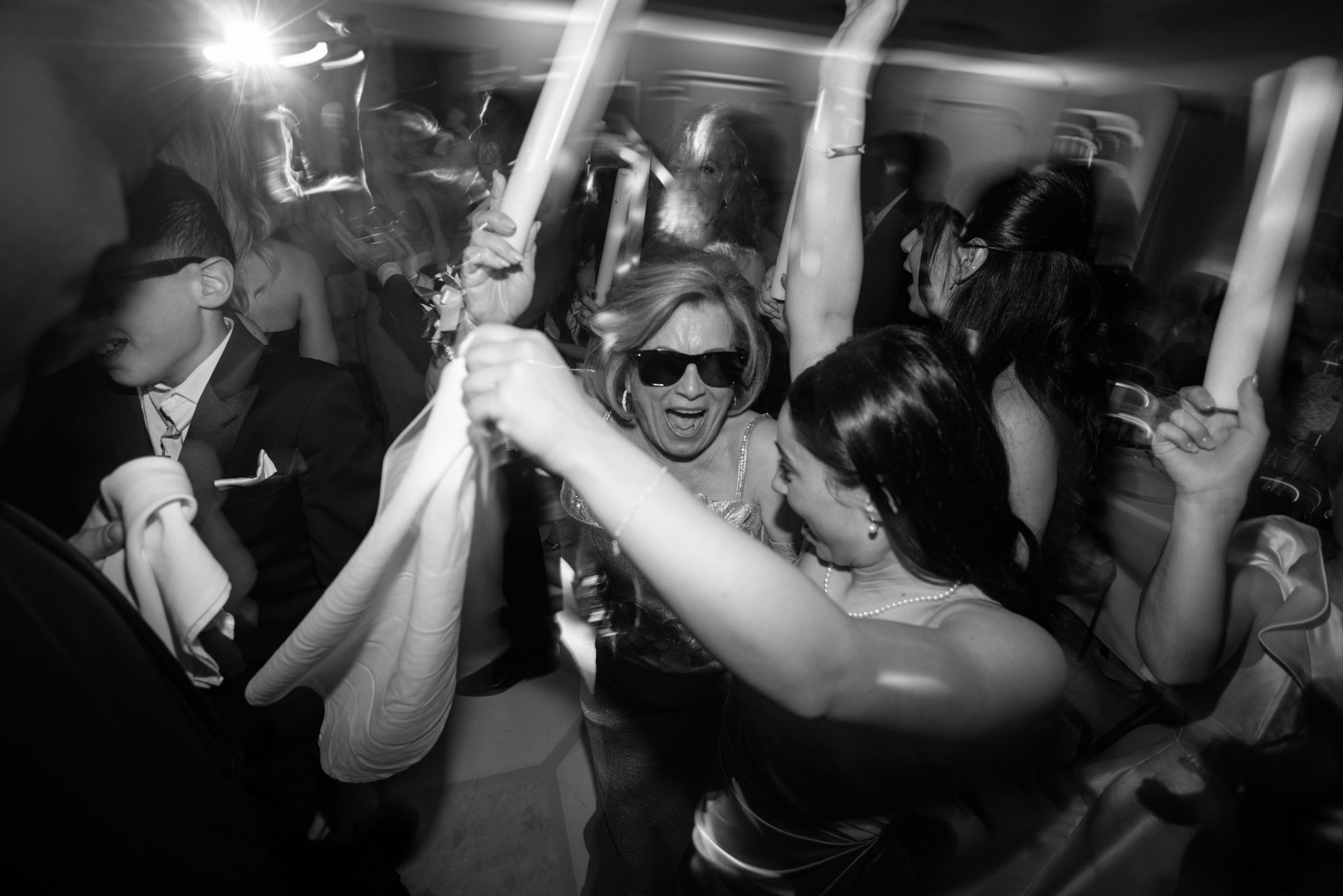 People dancing and celebrating at a party with glowsticks in a black and white photograph.