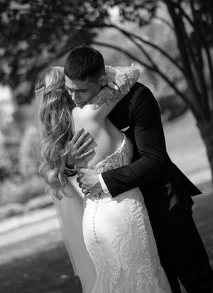 A romantic black and white wedding photo showing a couple embracing in an intimate moment outdoors.
