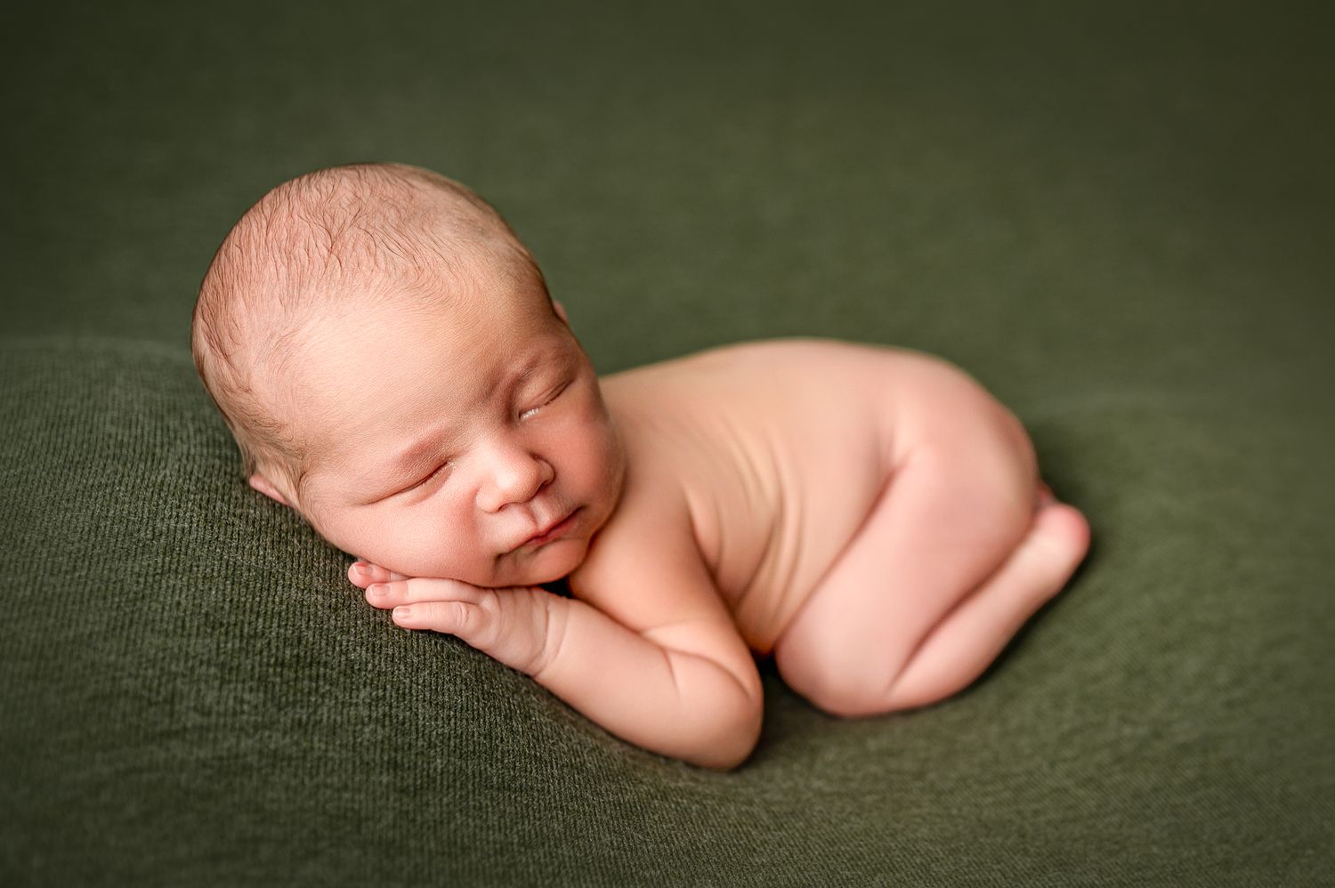 A sleeping newborn baby in soft lighting rests peacefully against a dark green background.