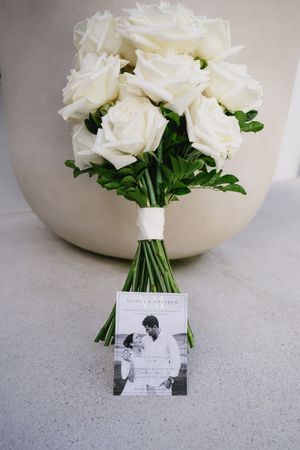 White rose wedding bouquet displayed with a vintage black and white photograph on a light gray surface.