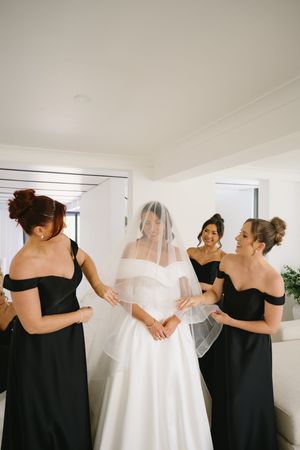 Candid moments of bridesmaids in black dresses assisting and embracing a bride in a white wedding dress.