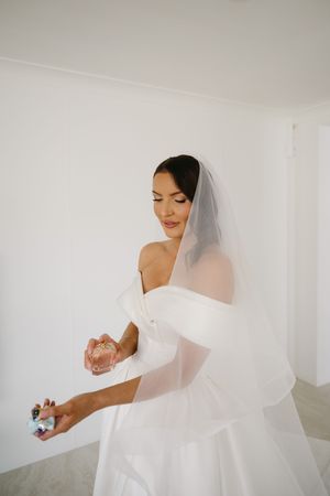 A bride in a white wedding dress and veil poses elegantly in a bright, minimalist room.
