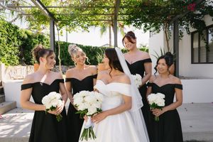 Wedding party in black and white dresses holding bouquets in a sunny outdoor garden setting.