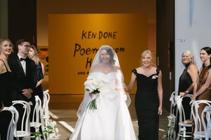 Wedding party lined up in formal attire against a bright yellow museum wall with text.