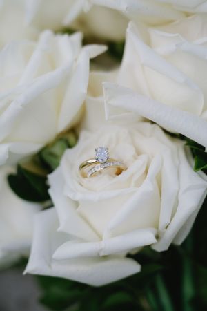 A diamond engagement ring nestled in the petals of a white rose with soft focus background.